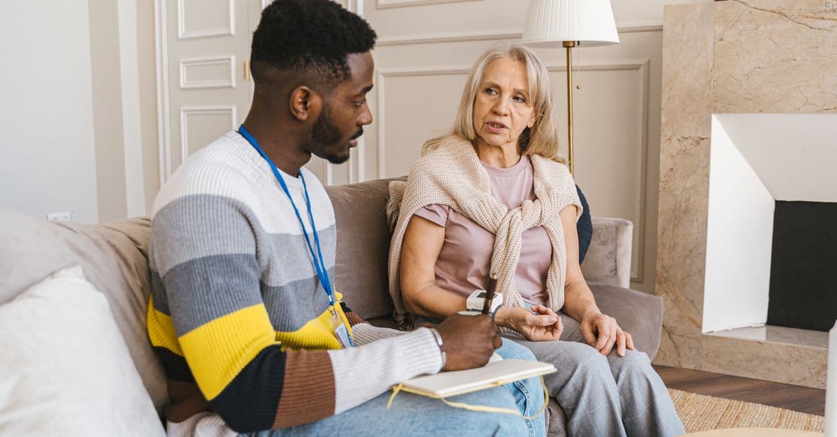 A caregiver listening attentively to a resident in a warm, sunlit living room.